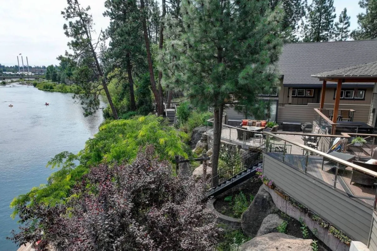 A serene riverside deck offers open views of the river, framed by mature trees and manicured landscaping. The deck is positioned for both relaxation and activity, perfect for launching kayaks or simply soaking in the peaceful surroundings. The natural setting emphasizes the property’s direct river access and outdoor adventure possibilities.
