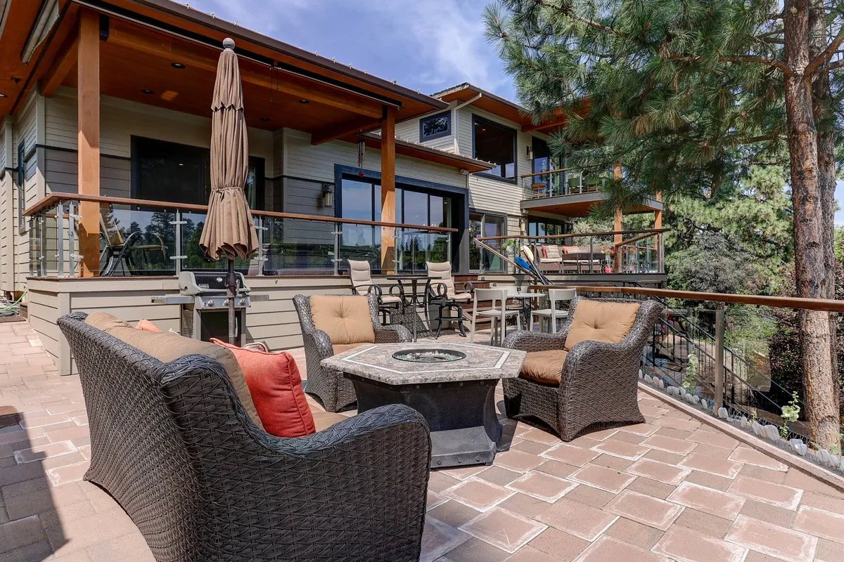 An exterior shot featuring a cozy outdoor seating area centered around a fire pit, flanked by lush greenery and the estate's large windows. The mood is serene yet social, perfect for starlit evenings, barbecues, or relaxed conversations after a day of activities.
