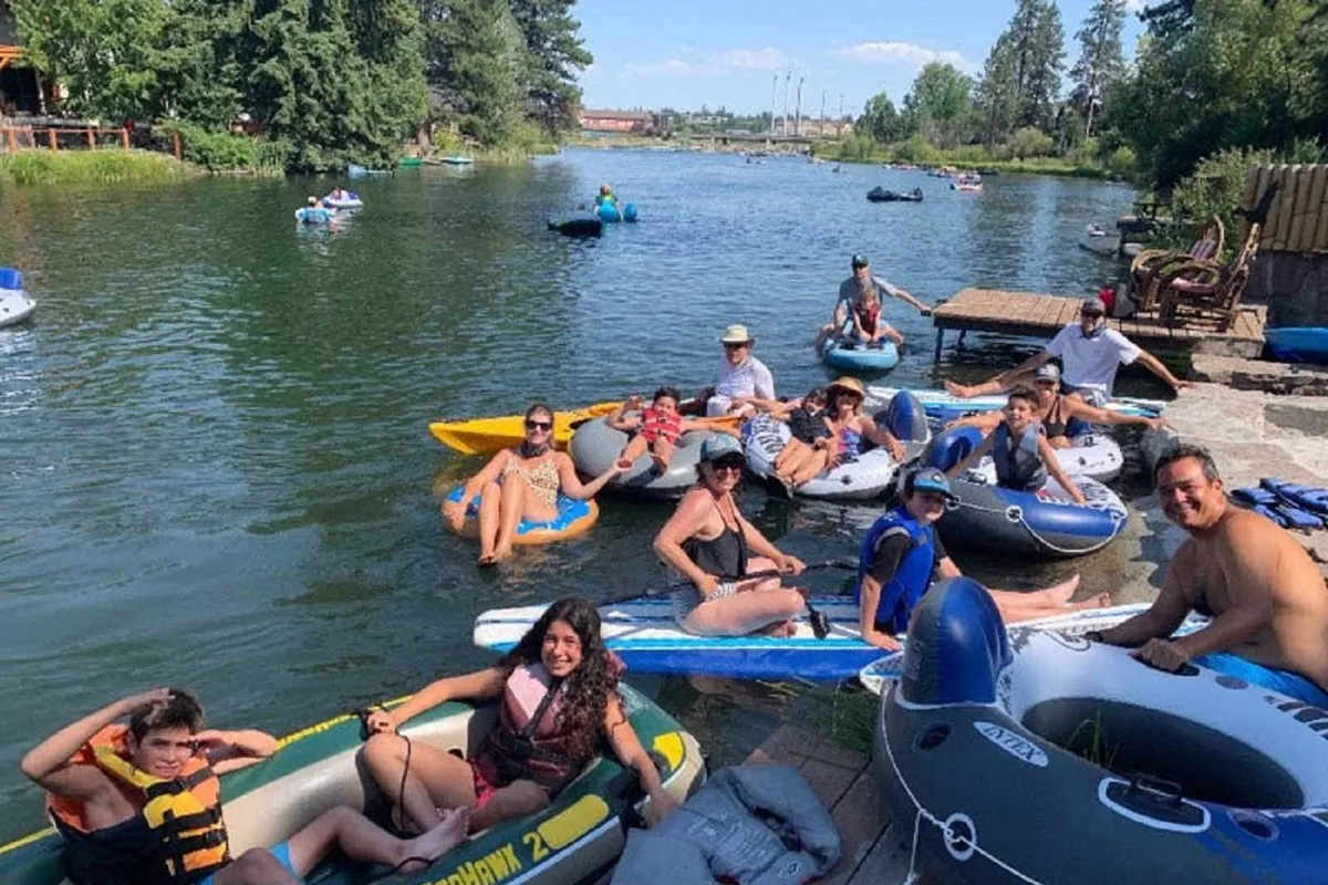 A lively scene featuring a group of people in inflatable boats floating on the river near a dock, surrounded by lush trees. The mood is energetic and carefree, capturing the excitement of spontaneous water adventures.