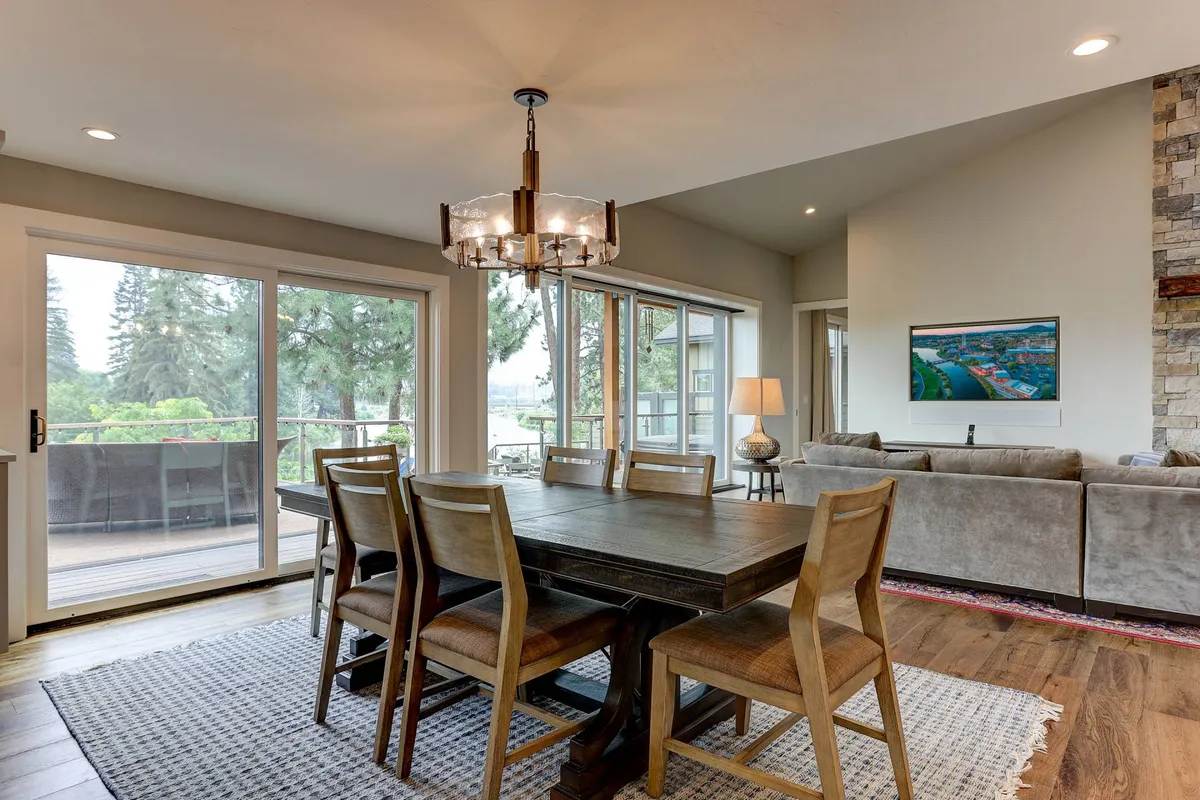 A well-lit dining area with a large table set near expansive windows that offer panoramic views of the surrounding landscape. Adjacent to a comfortable sofa and decorated with artistic touches, the space feels both sophisticated and welcoming, perfect for memorable meals and lively conversation.