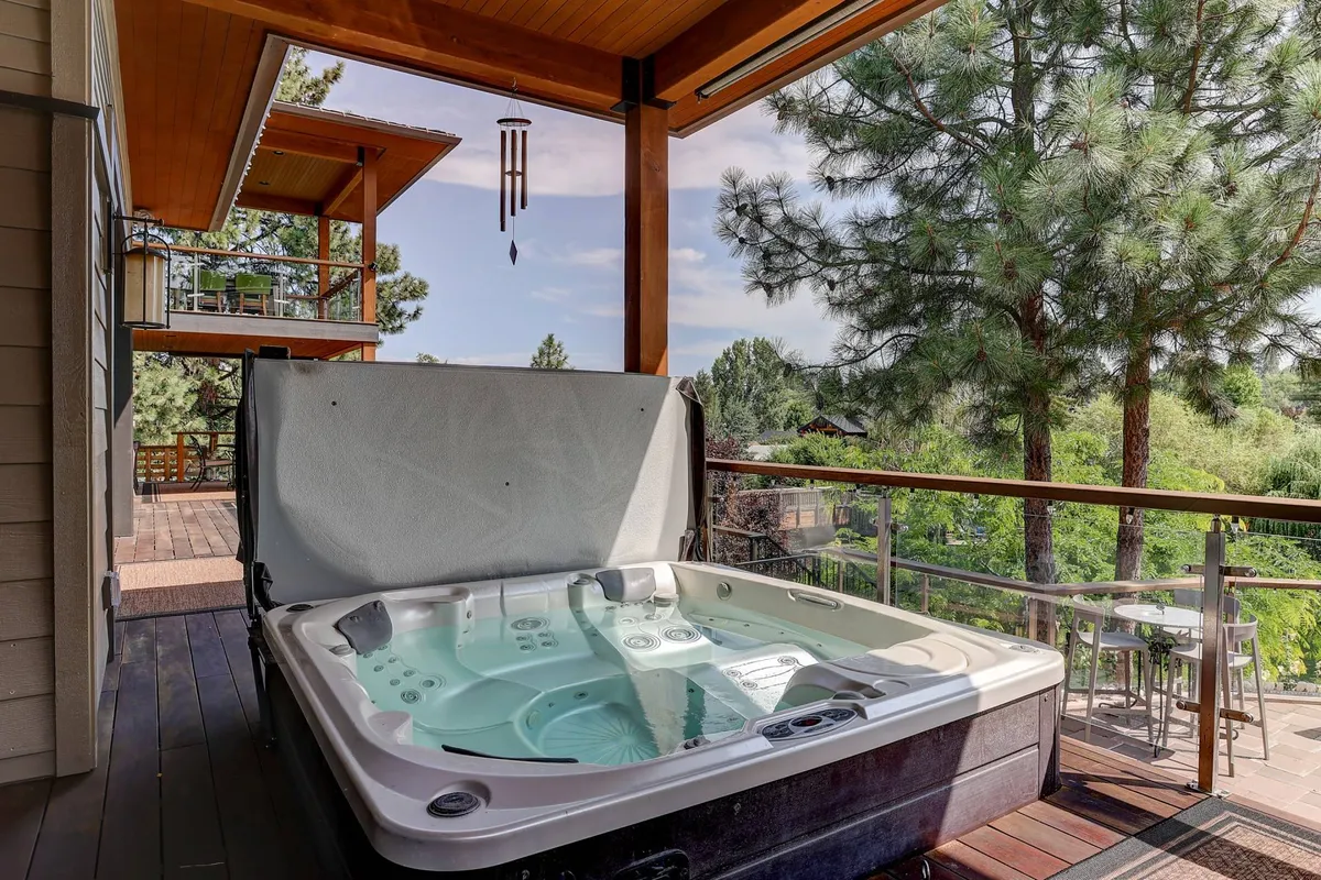 A tranquil deck area with a riverfront hot tub set among the trees, offering a peaceful spot to relax and unwind while enjoying natural views. The atmosphere is serene, suggesting comfort after a day outdoors.